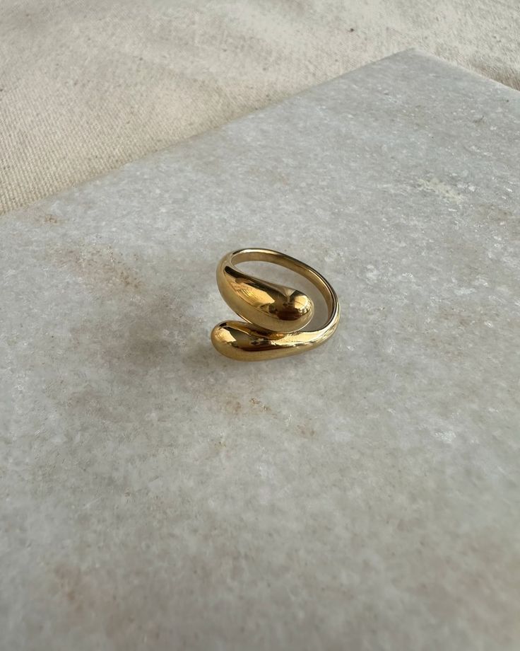 Anel Gota 18K em aço cirúrgico banhado a ouro, com design fluido em forma de gota e acabamento polido brilhante, sobre fundo branco minimalista.