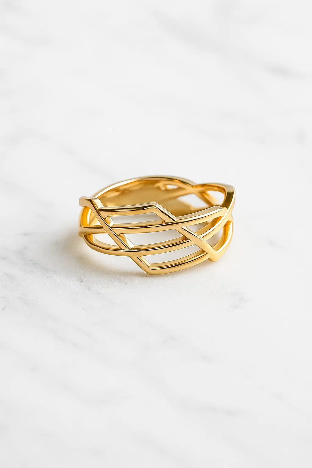 Anel dourado de aço cirúrgico banhado a ouro 18K, com design geométrico entrelaçado, formado por fios finos que se cruzam, fotografado sobre superfície neutra clara.