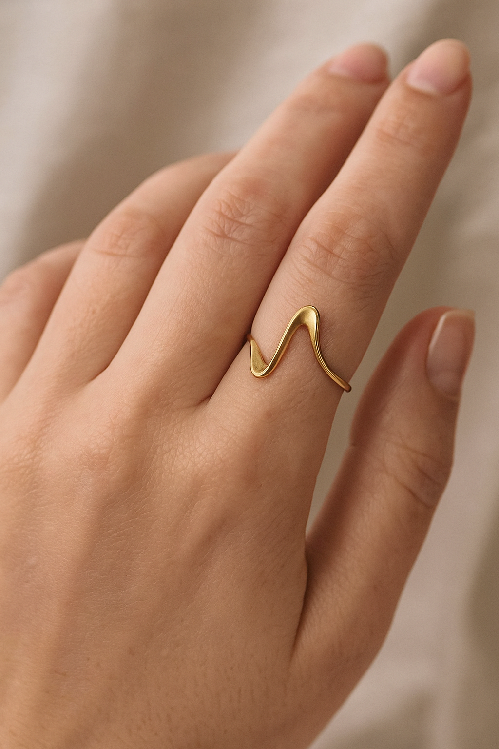 Anel Ripple 18K de aço cirúrgico banhado a ouro com design fino, ondulado e polido, formando curvas suaves e elegantes.