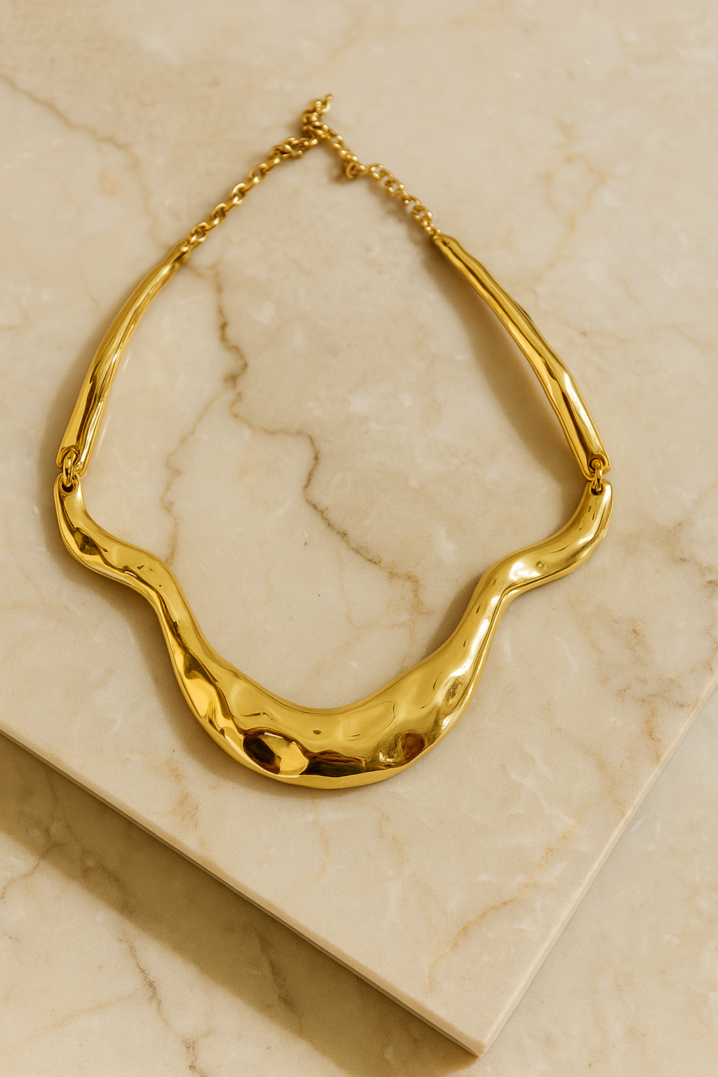 Colar dourado maxi com formas onduladas e acabamento polido, estilo escultural, fotografado sobre fundo branco.