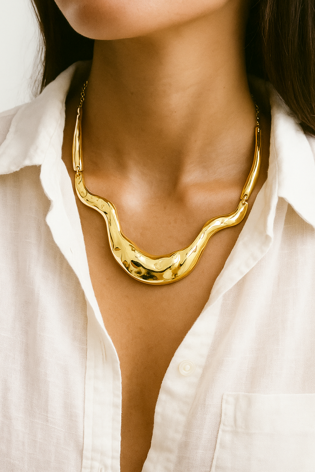 Colar dourado maxi com formas onduladas e acabamento polido, estilo escultural, fotografado sobre fundo branco.