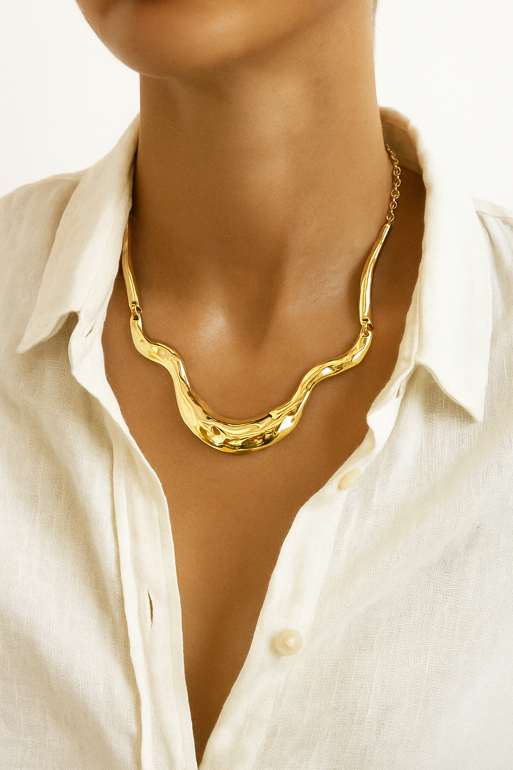 Colar dourado maxi com formas onduladas e acabamento polido, estilo escultural, fotografado sobre fundo branco.