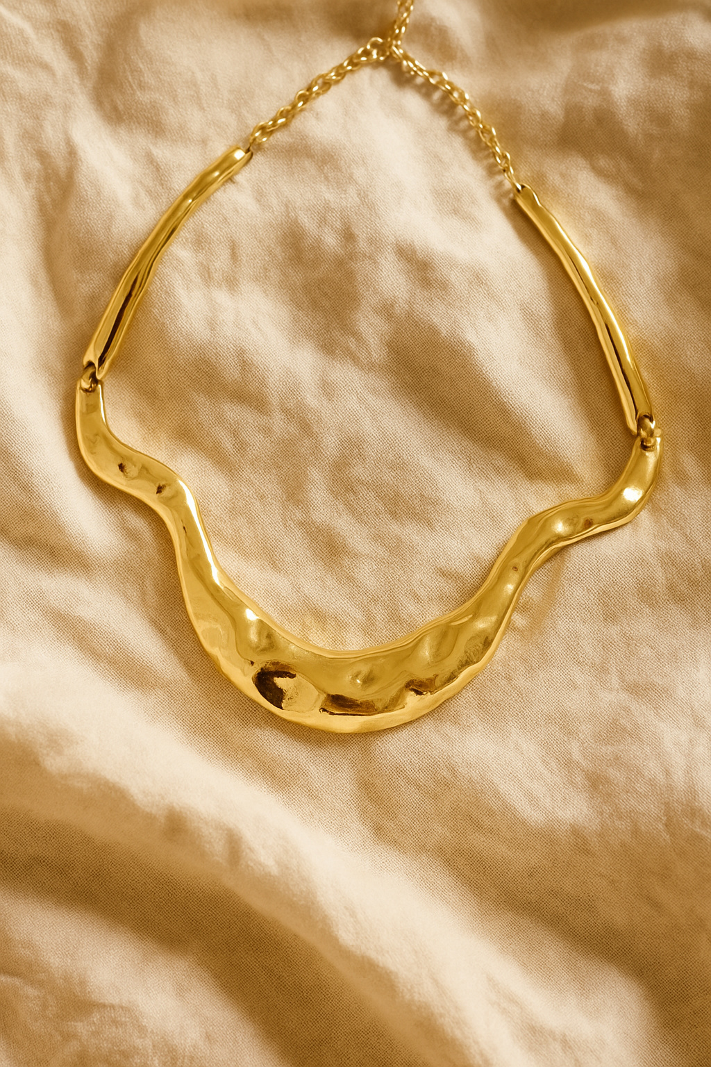Colar dourado maxi com formas onduladas e acabamento polido, estilo escultural, fotografado sobre fundo branco.