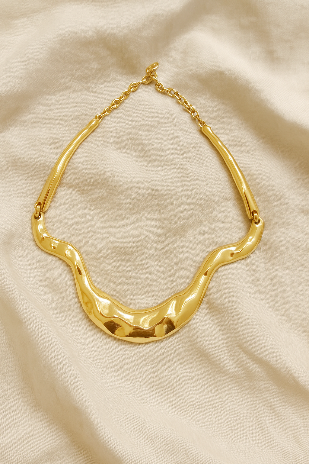 Colar dourado maxi com formas onduladas e acabamento polido, estilo escultural, fotografado sobre fundo branco.