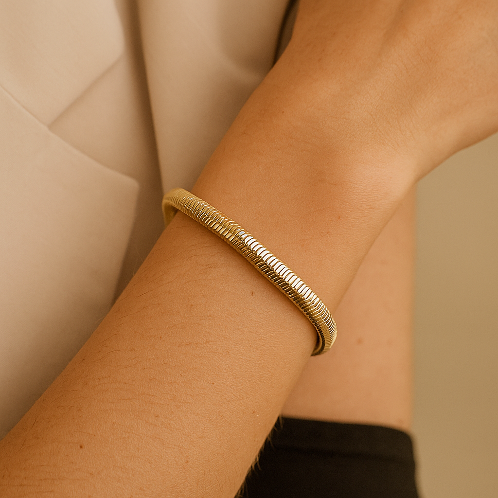 Pulseira dourada com malha flexível estilo "cobra", acabamento brilhante e fecho ajustável com corrente extensora e pingente circular, exibida sobre fundo branco.