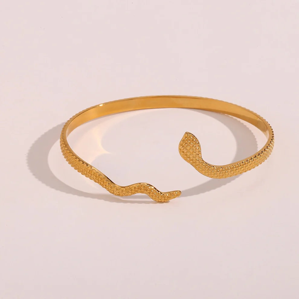 Pulseira rígida dourada com design de serpente estilizada, acabamento texturizado e abertura frontal em formato de cabeça e cauda de cobra, sobre fundo branco.