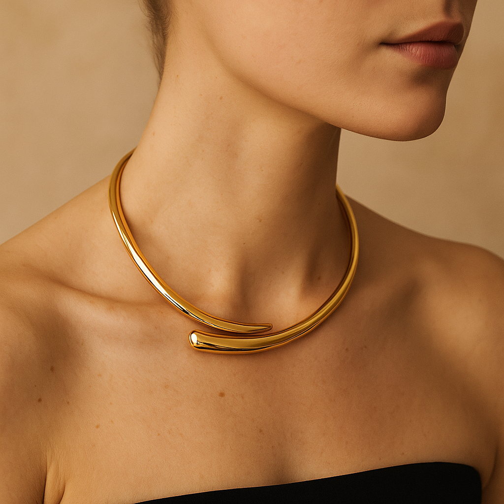 Colar rígido banhado a ouro 18K, com formato de meia-lua aberta e acabamento polido espelhado, posicionado ao redor do pescoço de uma modelo com top preto e fundo bege neutro.