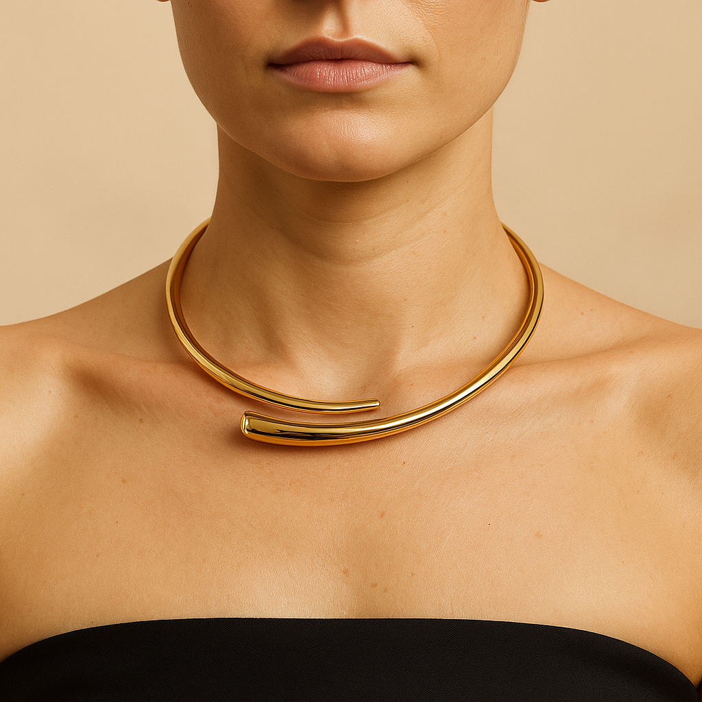 Colar rígido banhado a ouro 18K, com formato de meia-lua aberta e acabamento polido espelhado, posicionado ao redor do pescoço de uma modelo com top preto e fundo bege neutro.