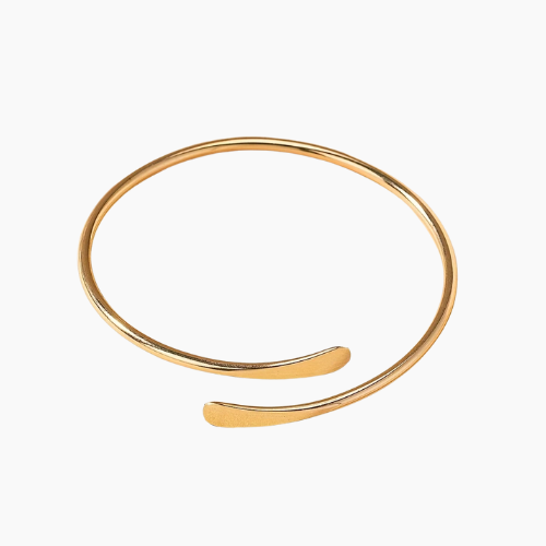 Pulseira minimalista banhada a ouro com design fino e acabamento polido, aberta nas extremidades com pontas suavemente arredondadas e levemente achatadas, exibida sobre fundo branco.